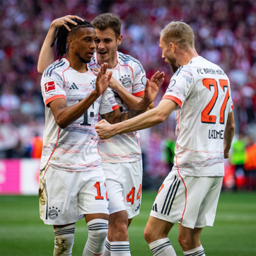 Rasmda Bayern Munich futbolchilari g'alaba qozongach, bir-birlariga quchishib, qiziqish va baxt hissi bilan nishonlashmoqda. Futbolchilar jamoa formasida, keng stadionda yig'ilgan muxlislar uchun qiziqarli muhit yaratilgan.